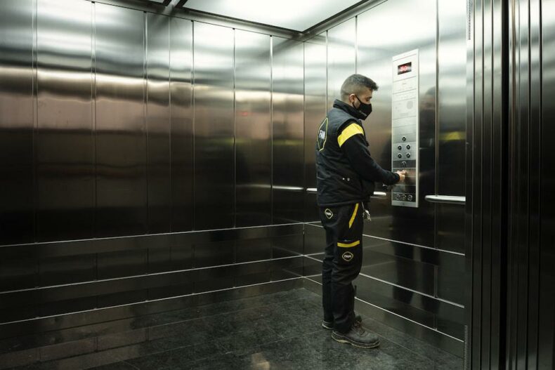 Technicien FAIN à l'intérieur d'un ascenseur en touchant la boite à boutons.